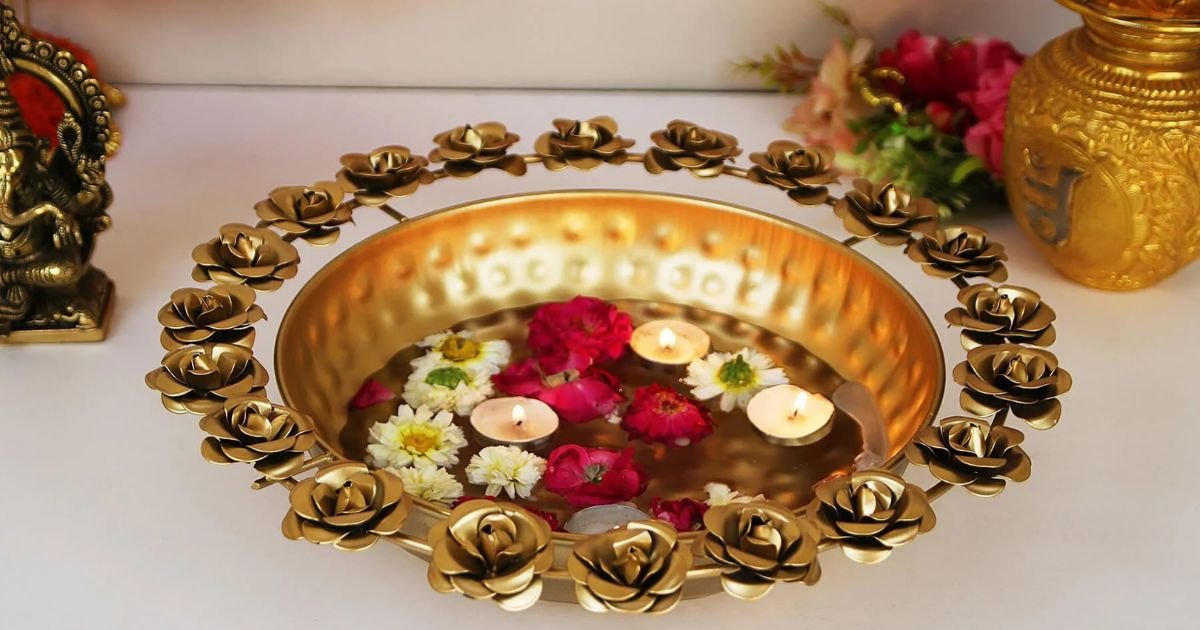 Brass ceremonial bowl with floating candles and flowers, encircled by a gold rose garland on a white table.