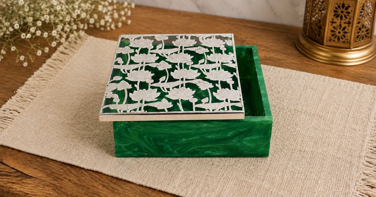 Green marble-style box with a silver floral lattice lid on a beige mat on a wooden table, decorative still life.