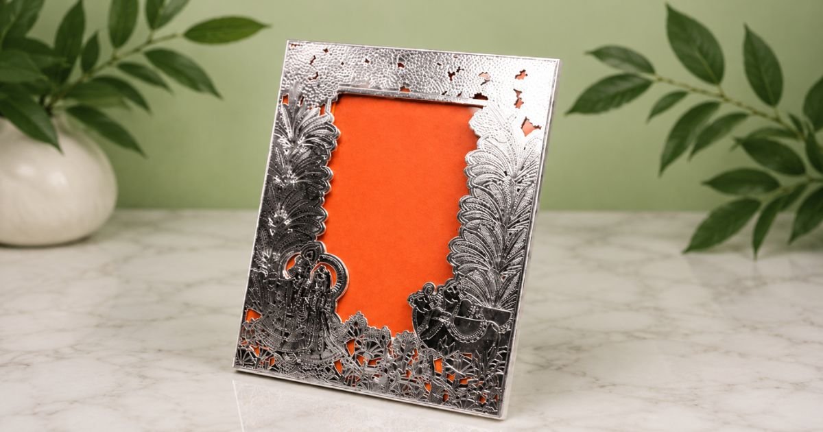 Ornate silver picture frame with intricate floral and landscape cutouts and an orange backing.