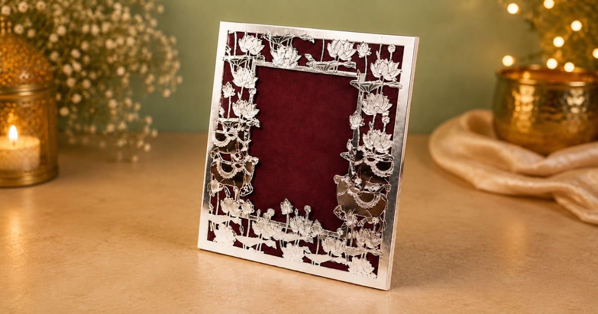 Ornate silver floral photo frame with a burgundy mat on a gold surface, candlelight and warm bulbs in the background.
