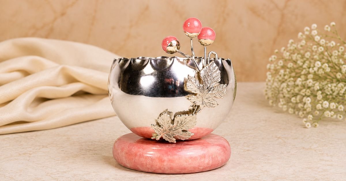 Polished silver decorative bowl with a pink stone base, carved maple leaves and pink-tipped orb accents, set on a pink stand.