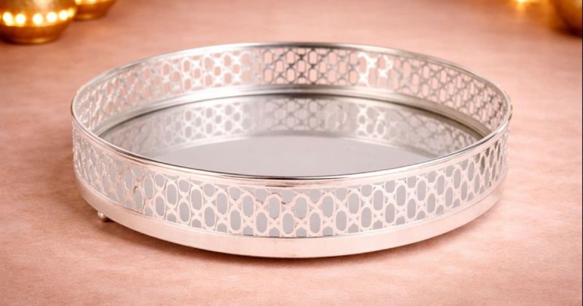 Round silver serving tray with decorative perforated lattice rim on a pink surface.