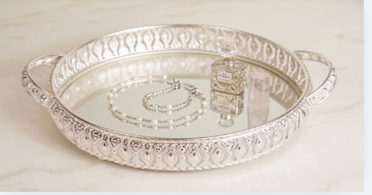 Ornate round silver tray with mirror base, displaying a perfume bottle, a crystal prism, and a bracelet.