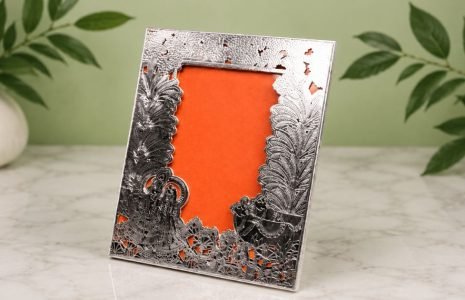 Ornate silver picture frame with intricate floral and landscape cutouts and an orange backing.