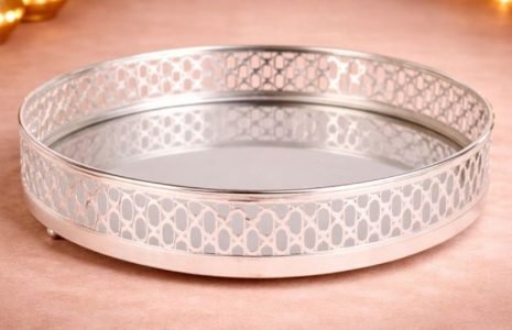 Round silver serving tray with decorative perforated lattice rim on a pink surface.
