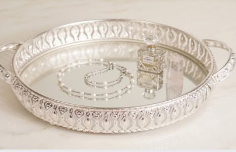 Ornate round silver tray with mirror base, displaying a perfume bottle, a crystal prism, and a bracelet.