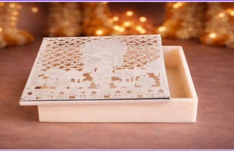 IVORY jewelry box with an intricate lace-pattern lid, partially open on a brown surface with warm holiday lights in the blurred background.