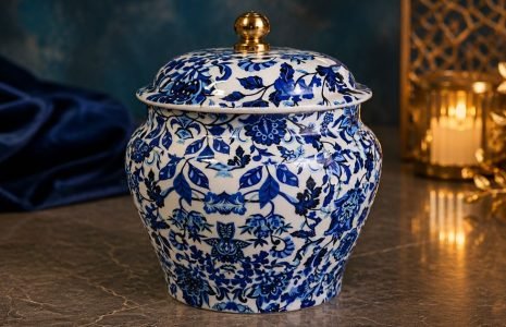 Blue and white porcelain jar with lid and gold knob on a marble surface, featuring an intricate floral pattern.